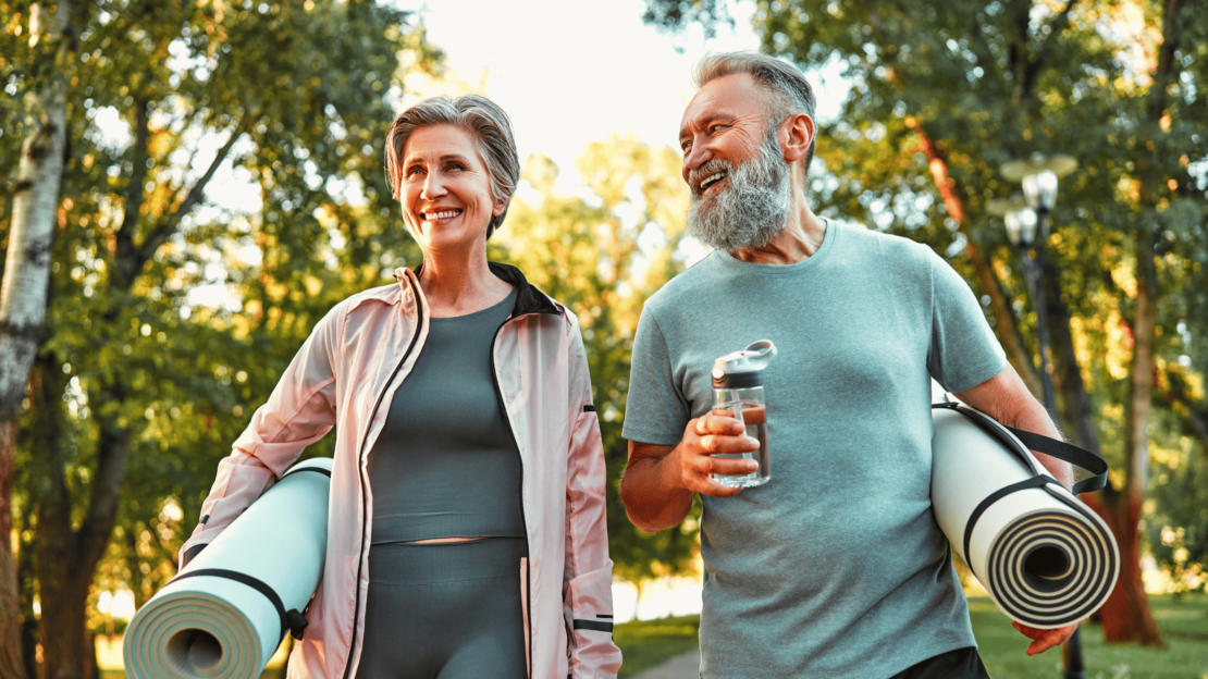 Senior man and woman smiling after chair yoga class, holding yoga mats and water bottles, enjoying the health benefits of chair yoga for seniors.