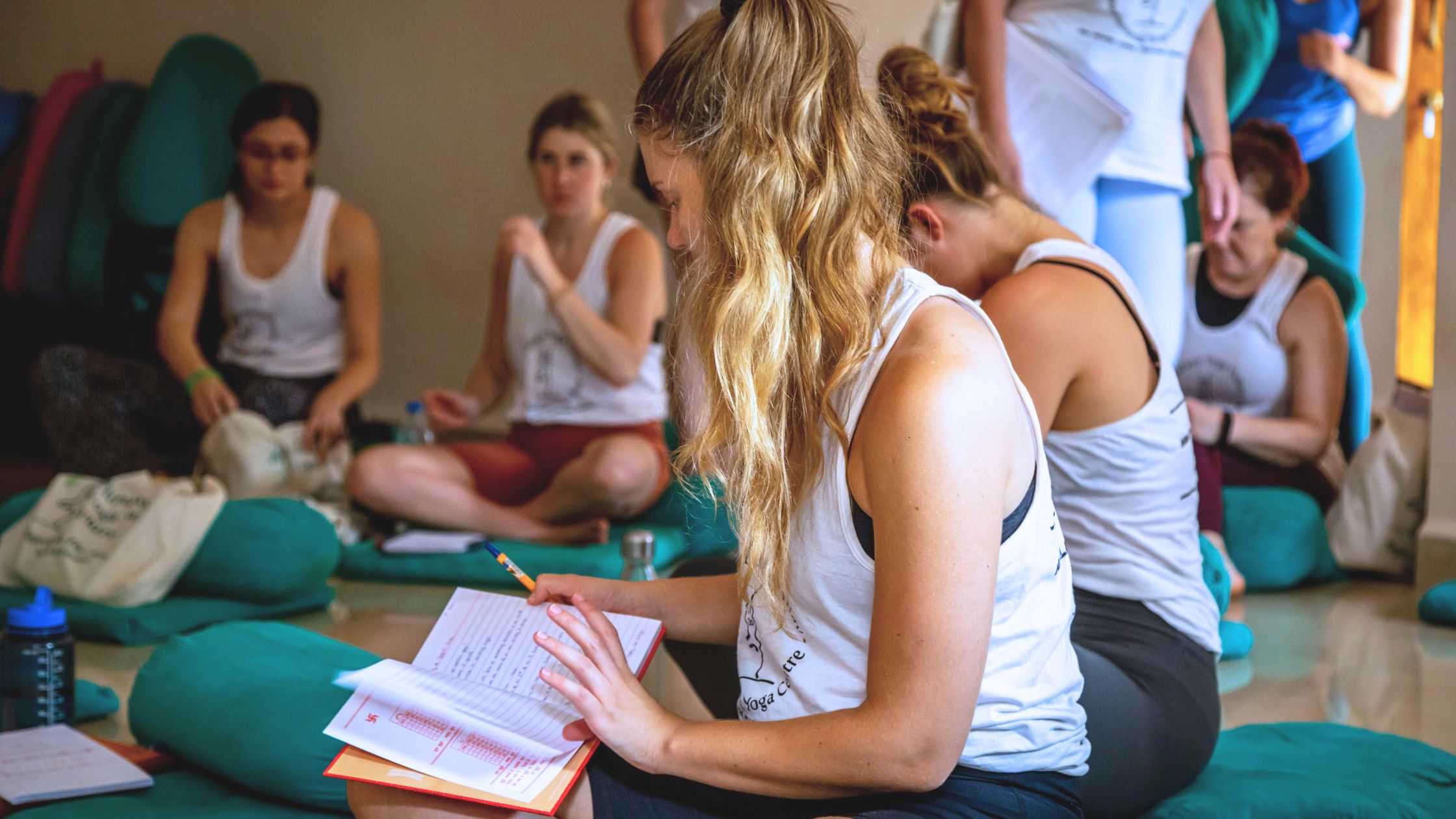 Woman writing in journal after yoga session, reflecting on her teacher training journey.