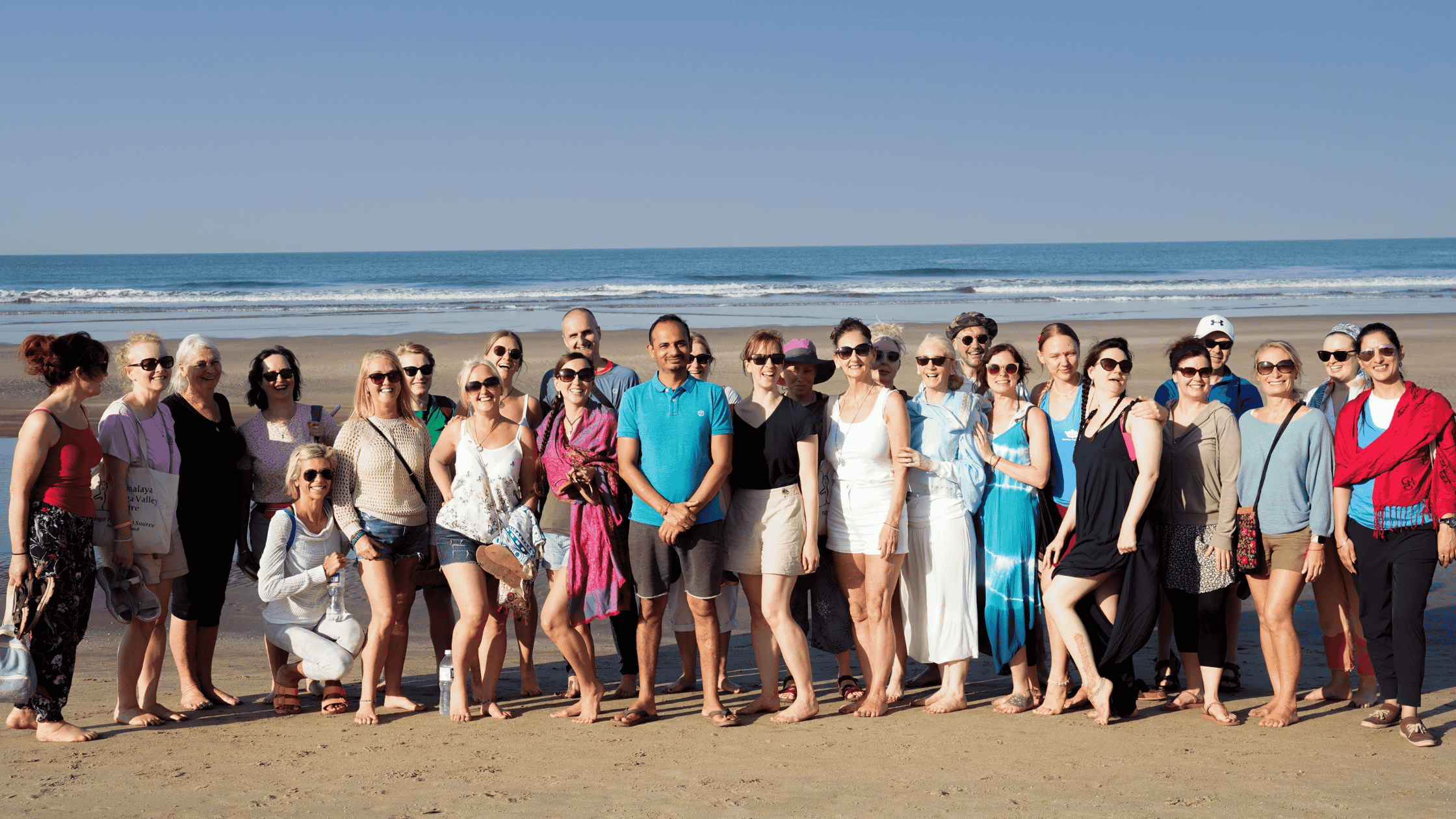 A group of Yogis have fun and find a sense of community during a Yoga Retreat in India, taking pictures at the beach.